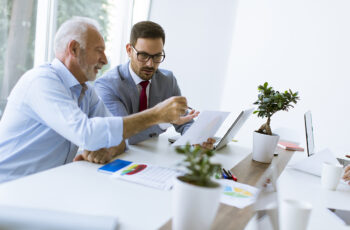 Handsome senior and young  businessmen  using a laptop, examining documents and discussing affairs while working in office